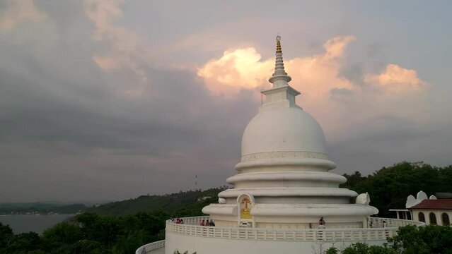 White pagoda buddhist temple among the jungle against the sunset clouds. Japanese Peace Pagoda in Sri Lanka aerial view.