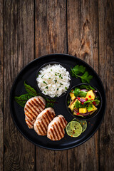 Grilled pork loin steaks with boiled white rice and mango salad on wooden table
