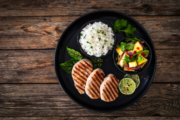 Grilled pork loin steaks with boiled white rice and mango salad on wooden table
