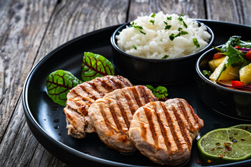 Grilled pork loin steaks with boiled white rice and mango salad on wooden table
