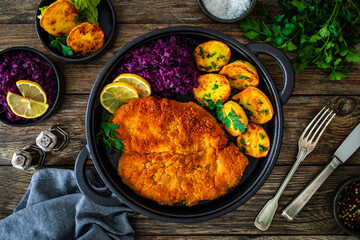 Crispy breaded fried cutlet with baked potatoes and cooked red cabbage on wooden table
 - obrazy, fototapety, plakaty