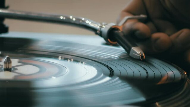 Close-up of a hand which changing song on a vinyl record by moving the turntable needle on a vintage record player. Concept of warm indoor atmosphere of enjoying music