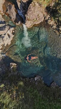 Ascending vertical shot of a woman in swimsuit swims the Fairy Pools on the Isle of Skye, Scotland