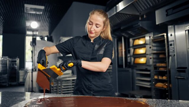 A confectioner tempers chocolate before preparing desserts using metal spatula on kitchen surface