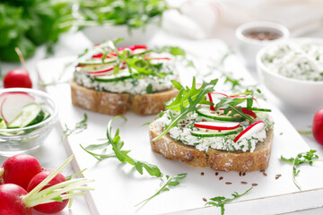 Sandwiches with rye bread toasts, cottage cheese, radish, cucumber, fresh greens and arugula for a healthy breakfast