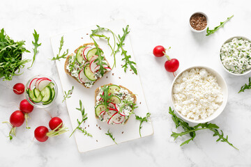 Sandwiches with rye bread toasts, cottage cheese, radish, cucumber, fresh greens and arugula for a healthy breakfast, top view - obrazy, fototapety, plakaty