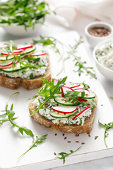 Obraz premium Sandwiches with rye bread toasts, cottage cheese, radish, cucumber, fresh greens and arugula for a healthy breakfast