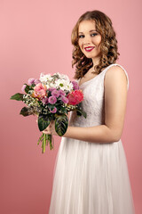 Bride in white wedding dress holds wedding flower in front of the light pink background