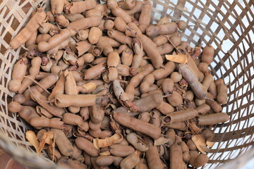 A fresh pile of ripe sweet tamarind is dried in the sun in a bamboo basket on an Asian fair in Thailand. A close-up of the tamarind in the basket.