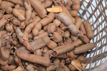 A fresh pile of ripe sweet tamarind is dried in the sun in a bamboo basket on an Asian fair in Thailand. A close-up of the tamarind in the basket.