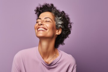 Happy young african american woman with curly hair laughing and looking up on purple background
