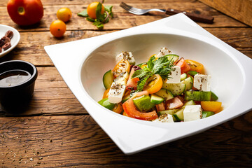 Mediterranean Salad with cucumber, tomato, basil and cheese cube served in dish isolated on wooden table with raw food top view of super healthy appetizer food