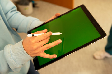 A hand with a stylus draws on a tablet with a green screen. Place for an inscription. Technology...