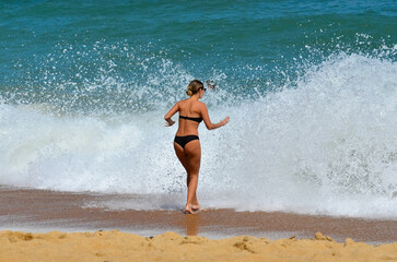 Slim girl in a swimsuit on the beach in front of a big wave,no recognizable people in the photo