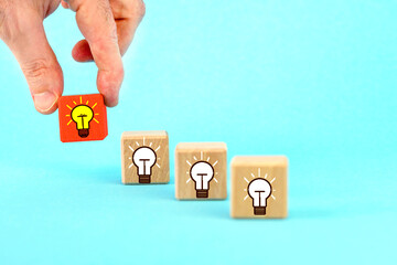  Wooden cubes with lightbulb icons on the background. Hand takes a cube with a light bulb symbol.