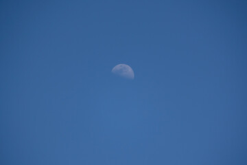 A view of the moon with blue sky in the daytime. 
