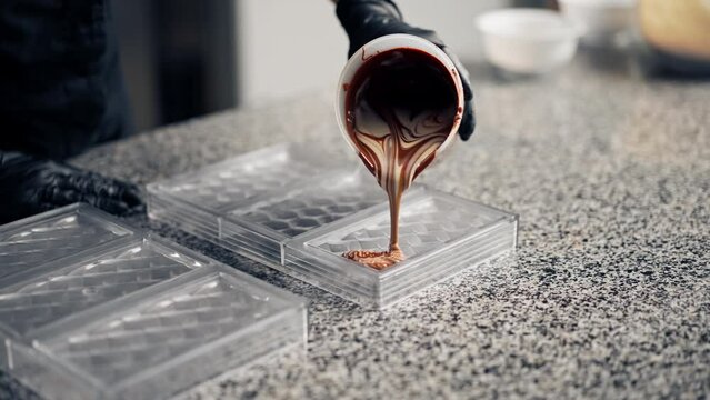 Close-up shot of a chocolatier pouring melted hot chocolate into clear chocolate mold for making candies