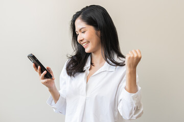 Fototapeta premium Happy asian young woman using mobile smart phone, read good news online feel excited getting offer, great positive surprise, celebrate success on smartphone. Businesswoman isolated on white background
