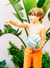 Caucasian blond 9 year old boy with a soccer ball in his hand while pointing with the other hand. Vertical.