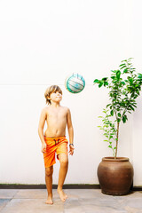 Caucasian blond 9-year-old boy doing tricks with a soccer ball. Vertical with copy space.
