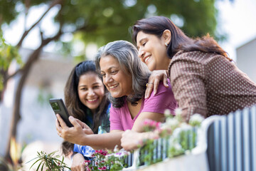 Three female friends laughing at something on a mobile phone while standing together outside in a back yard