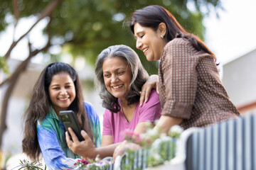 Three female friends laughing at something on a mobile phone while standing together outside in a back yard