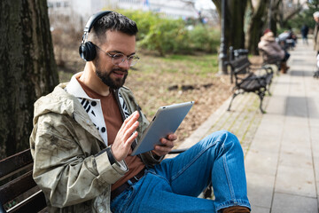 Young freelance hipster generation Z man sitting in park relaxing read emails checking business...