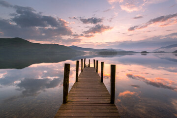 Beautiful sunset reflections on a calm Summer evening at Derwentwater with picturesque wooden jetty. Lake District, UK. - 738782994