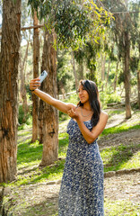 vertical photo latina woman taking a selfie with her cell phone in a forest in bolivia - tourism concept