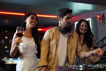 Disc jockey Dj mixing party in bar .Two young Asian and Caucasian friends dancing having fun...