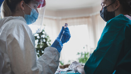 Doctors in protective suit vaccinating elderly woman at home during epidemic