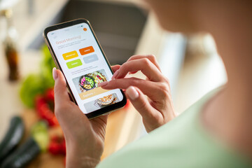 Young woman using recipe app on smartphone for preparing meal at home