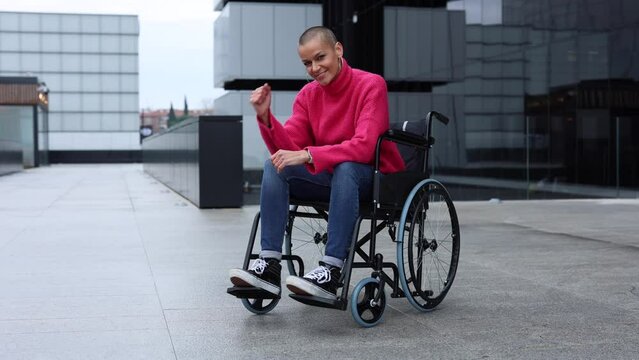 women we can. Modern bald athlete posing looking at the camera in her wheelchair smiling and optimistic while raising her fist: empowerment and cancer survivor