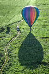 A multi-colored hot air balloon begins to fly on a green field. Next to the ball is a dirt road...