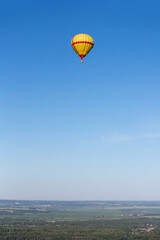 A yellow-red hot air balloon flies high in the sky over the countryside. Summer day. Balloon flight.