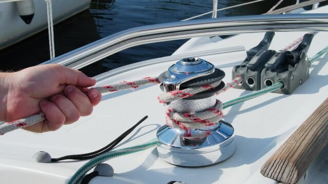 Seasoned yachtsman wraps nylon cable around drum controlling tension. Strong sailor prepares lines for safe sailing in sea