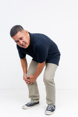 A middle aged asian man winces in pain. Bending down clutching his bum knee. Isolated on a white background.