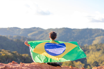 Brazilian seated atop a mountain, draped in the Brazilian flag, surrounded by a mountainous...