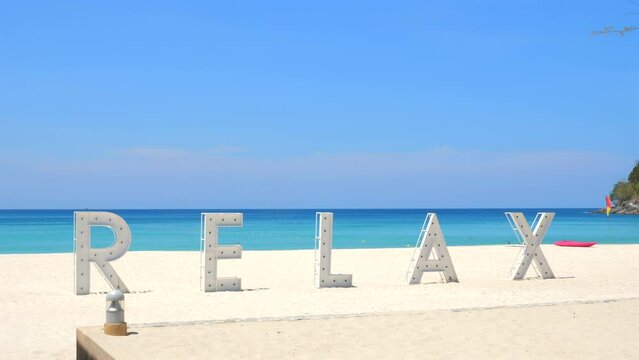 Serene beach scene with large 'RELAX' letters on white sand against backdrop of clear blue sky and turquoise sea. Vacation and travel.