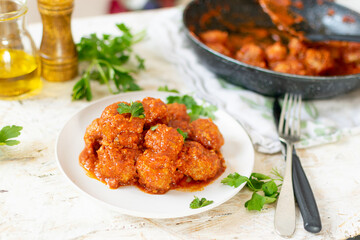 Classic Italian meatballs with tomato sauce on white plate and rustic background.