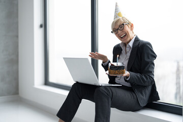 Business woman holding birthday cake and have video call