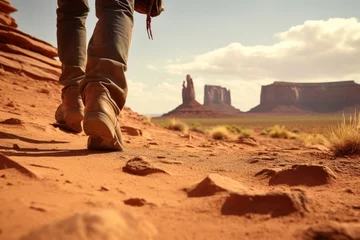 Gordijnen Ground level view of the foot of a cowboy walking on highway with Landscape of American’s Wild West with desert sandstones. © Joyce