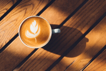 Latte art on a coffee cup with shadow on a wooden table from a high-angle view.