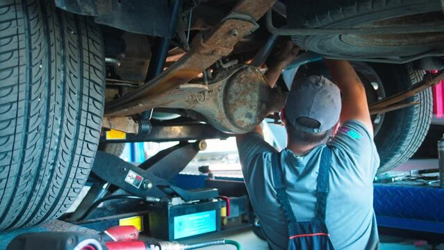 A diligent mechanic in a workshop, attentively working beneath a raised car, tools in hand, exemplifies the intricacies of vehicle upkeep