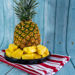 Pineapple slices on a black plate on a light blue wooden table. Healthy fruit.