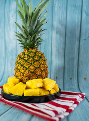 Pineapple slices on a black plate on a light blue wooden table. Healthy fruit.