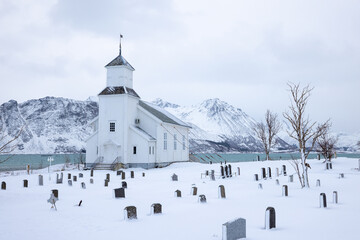 Gimsøysand church on Lofoten Islands in Norway in winter with snow capped mountains and cloudy skies