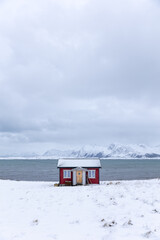 Red house at the sea with snow capped mountains on Lofoten Islands Norway