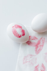 white Easter egg with a red lipstick print on a white background, next to it is a napkin with many lip prints and a blank white egg