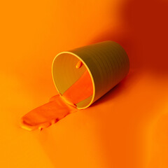 Orange paint in a plastic cup on an orange background. Copy space.